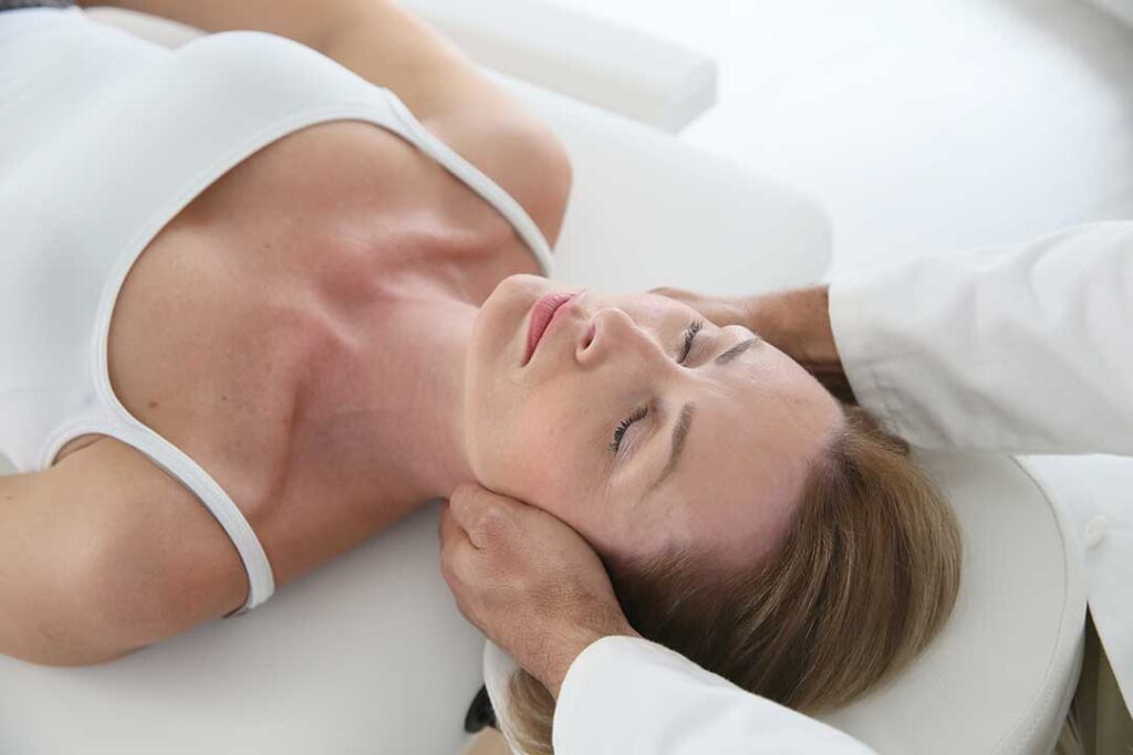 Person performing a gentle knee-to-chest stretch on a mat beside a bed in morning light.