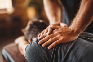 Chiropractor guiding an adult through gentle back mobility exercises in a bright treatment room.